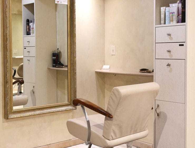 A salon interior with a chair facing a mirror and products on shelves.