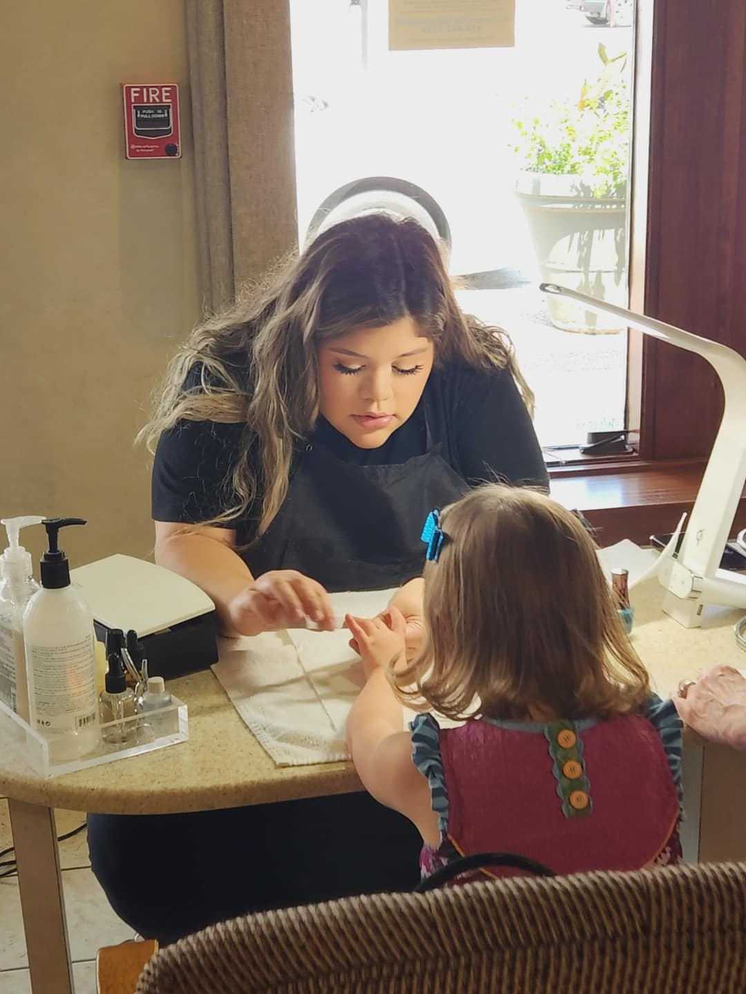 Woman giving a young girl a manicure at a nail salon.