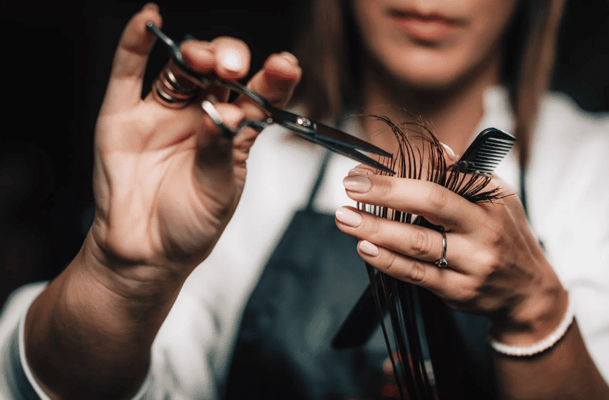 Close-up of hairdresser's hands trimming hair with scissors and comb.