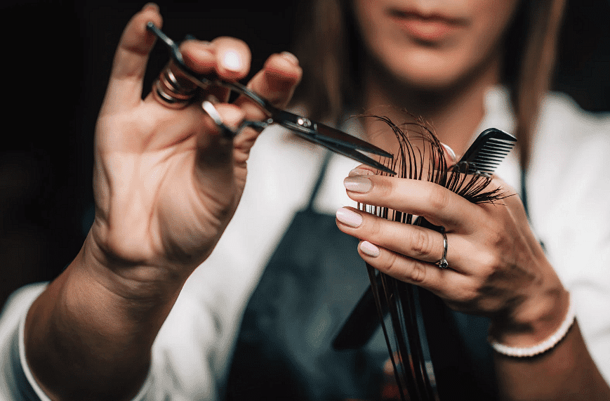 Close-up of hairdresser's hands trimming hair with scissors and comb.