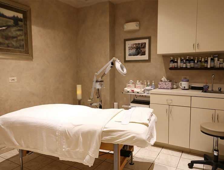 A cozy spa treatment room with a massage bed and shelves of products.