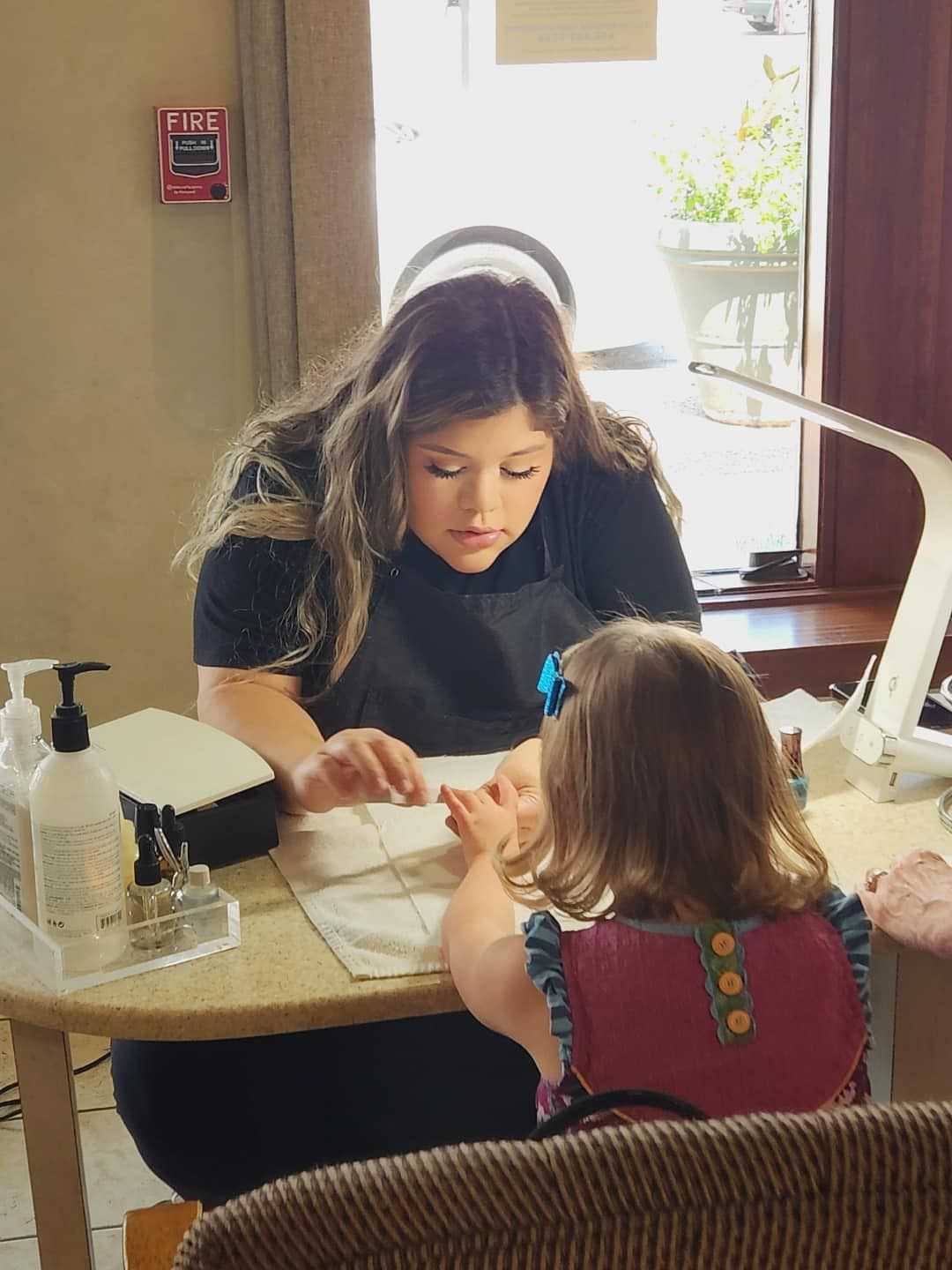 Woman giving a young girl a manicure at a nail salon.